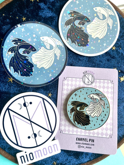 feature of two betta fish stickers, the matching enamel pin, and a shop sticker that reads, Nio Moon
