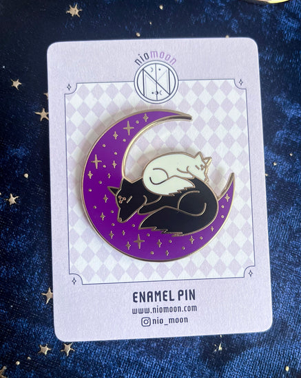 an enamel pin of the black and white dogs sleeping on a crescent moon placed on a back card display