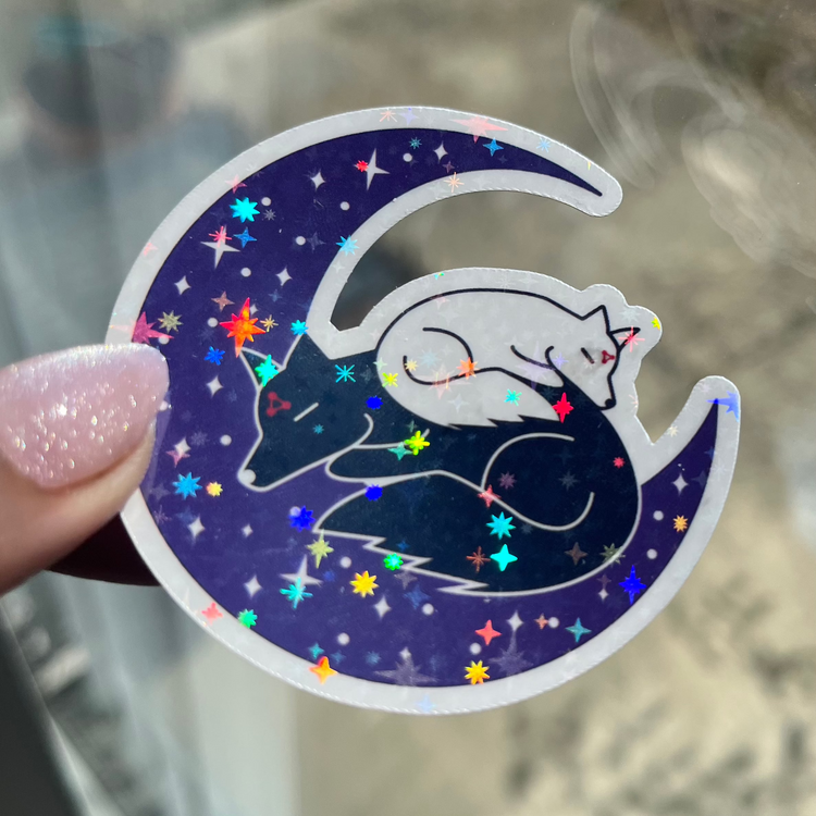 holographic sticker of black and white dogs sleeping on a crescent moon