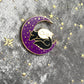 An enamel pin of the black and white dogs sleeping on a crescent moon