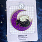 an enamel pin of the black and white dogs sleeping on a crescent moon placed on a back card display